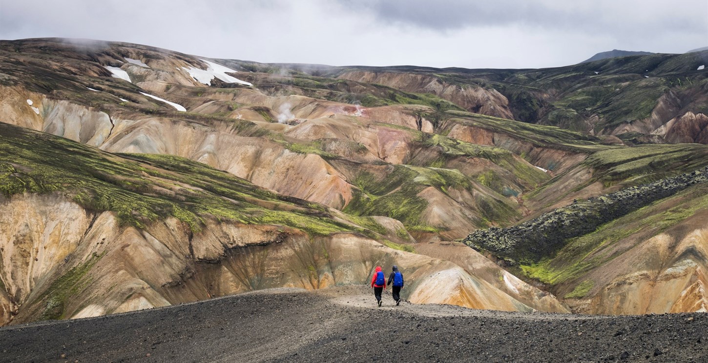 2 people hiking across natural mountains in Landmannalaugar, Iceland
