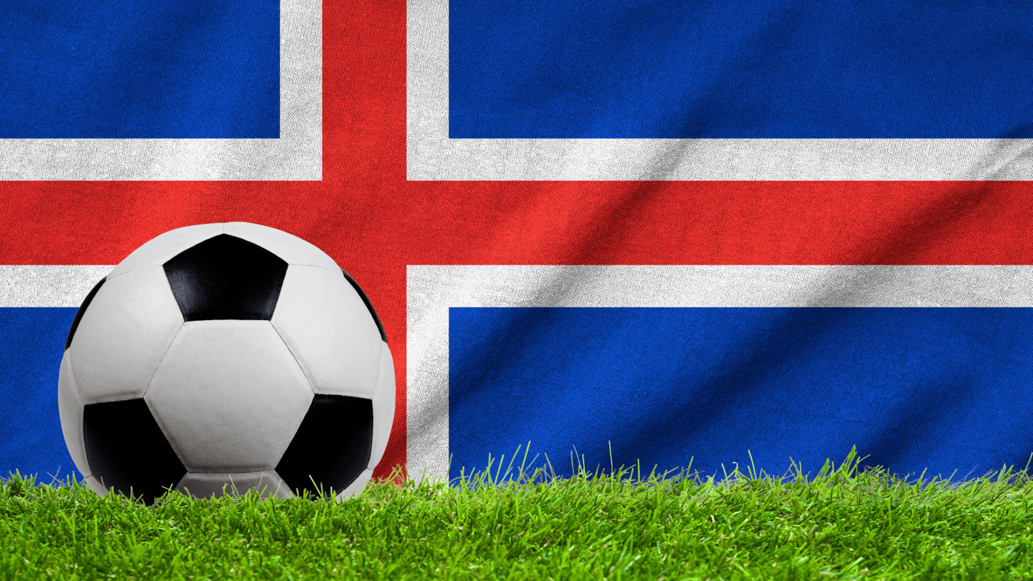 Football on a grassy field with the flag of Iceland in the background.