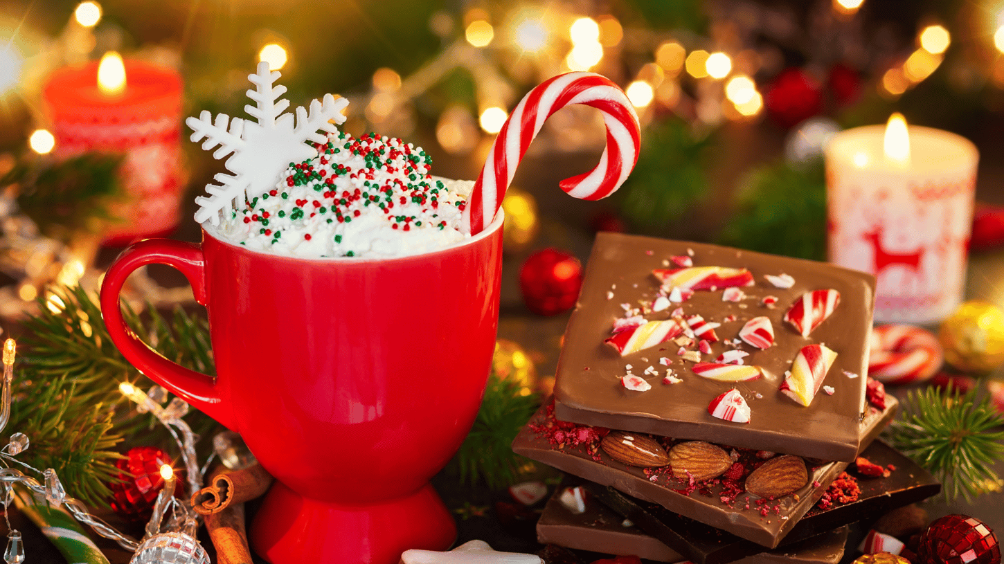 A red cup with whipped cream topped with colourful sprinkles, a snowflake, and a Christmas candy cane. 