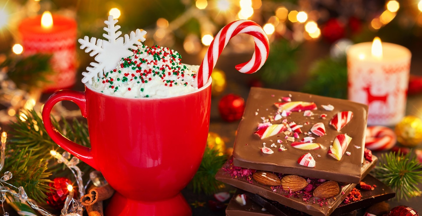 A red cup with whipped cream topped with colourful sprinkles, a snowflake, and a Christmas candy cane.