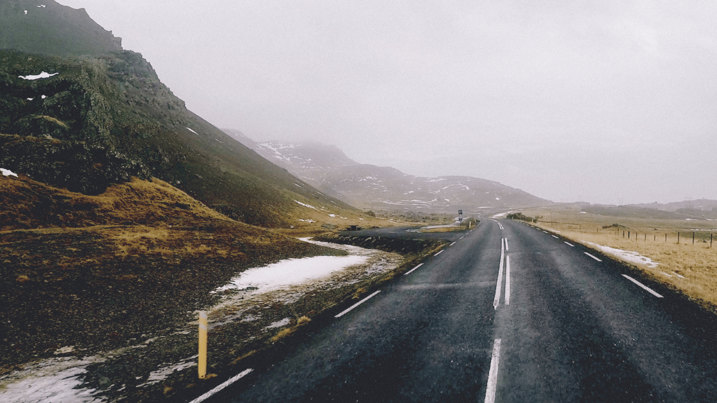 Road in Iceland beneath mist-topped grassy hills to the left.