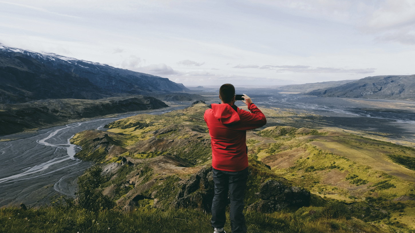 A man in a red coat taking a picture of the valleys in Þórsmörk