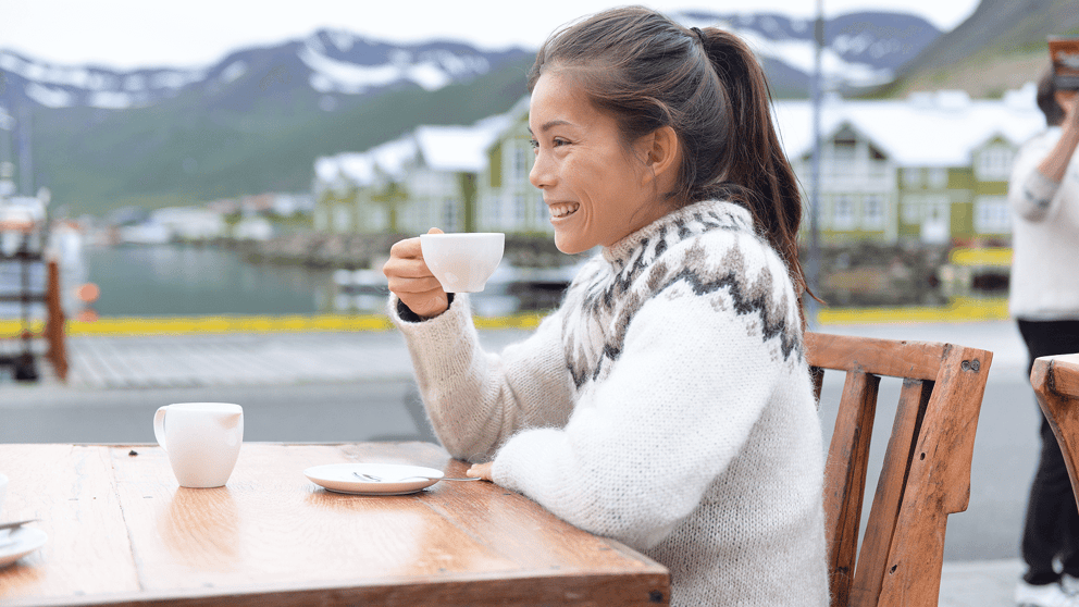 Woman in an Icelandic sweater sitting outside a cafe in Iceland drinking a cup of coffee.