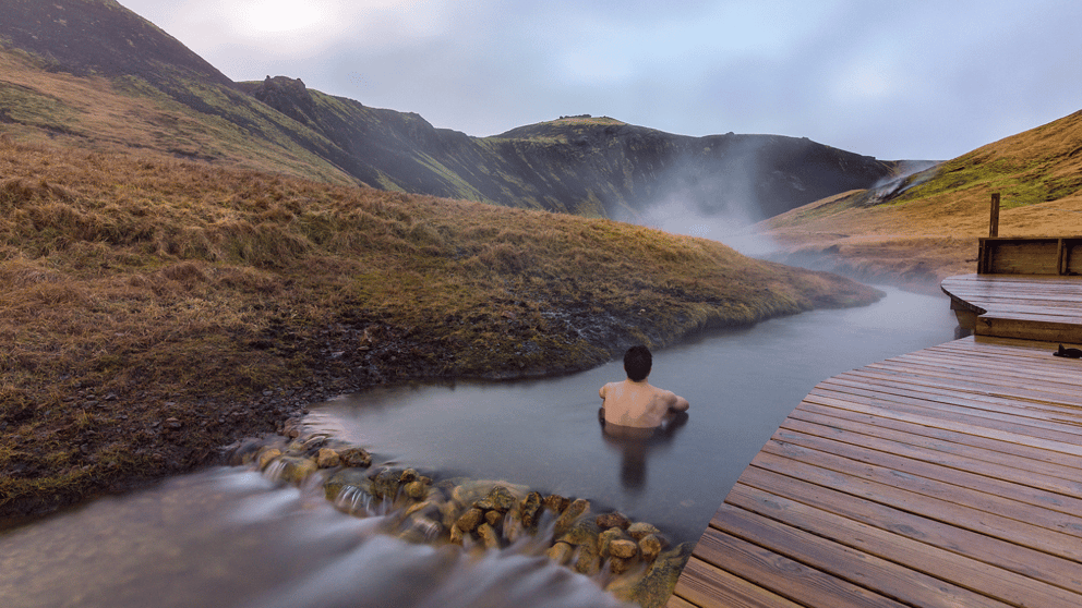 Man submerged in Reykjadalur Hot Spring beside the boardwalk.