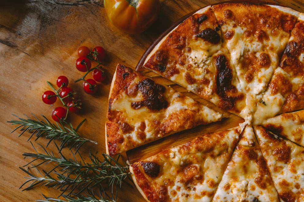 Close-up of pizza with fresh herbs and vegetables on a wooden table.