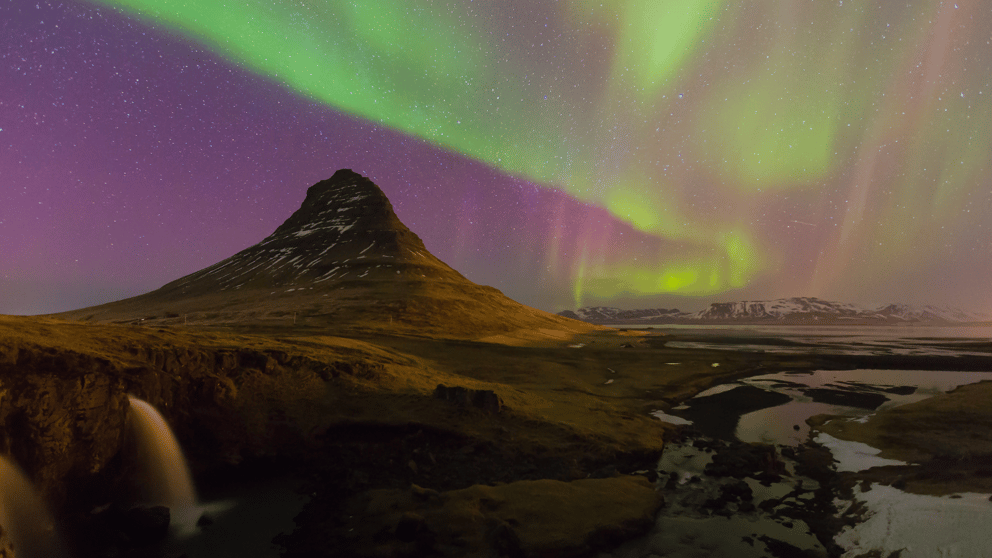 Purple and green Northern Lights moving over the Kirkjufell volcano in Iceland.