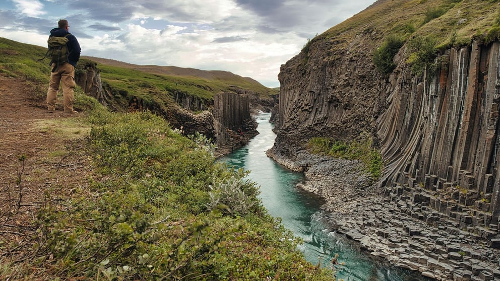 Hiker on the banks of the Jökulsá á Dal river in Studlagil Canyon.