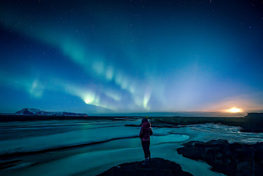 Woman standing on an Icelandic beach with the Northern Lights overhead