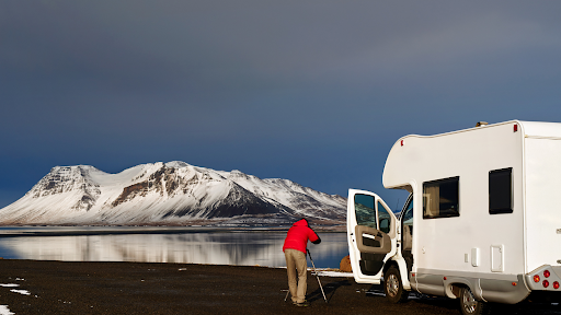 Traveller stood outside a campervan taking photos of snowy mountains