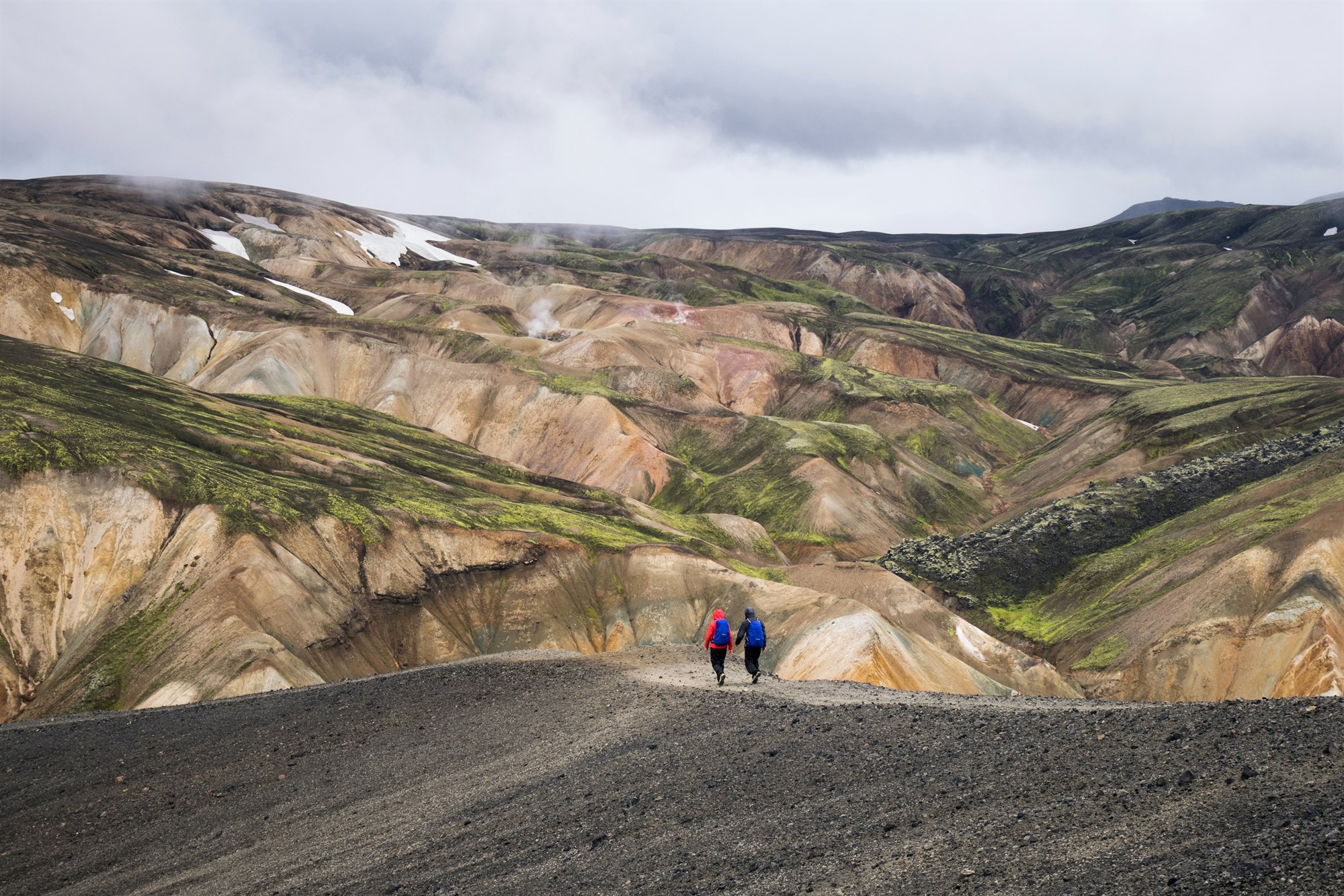 2 people hiking across natural mountains in Landmannalaugar, Iceland 