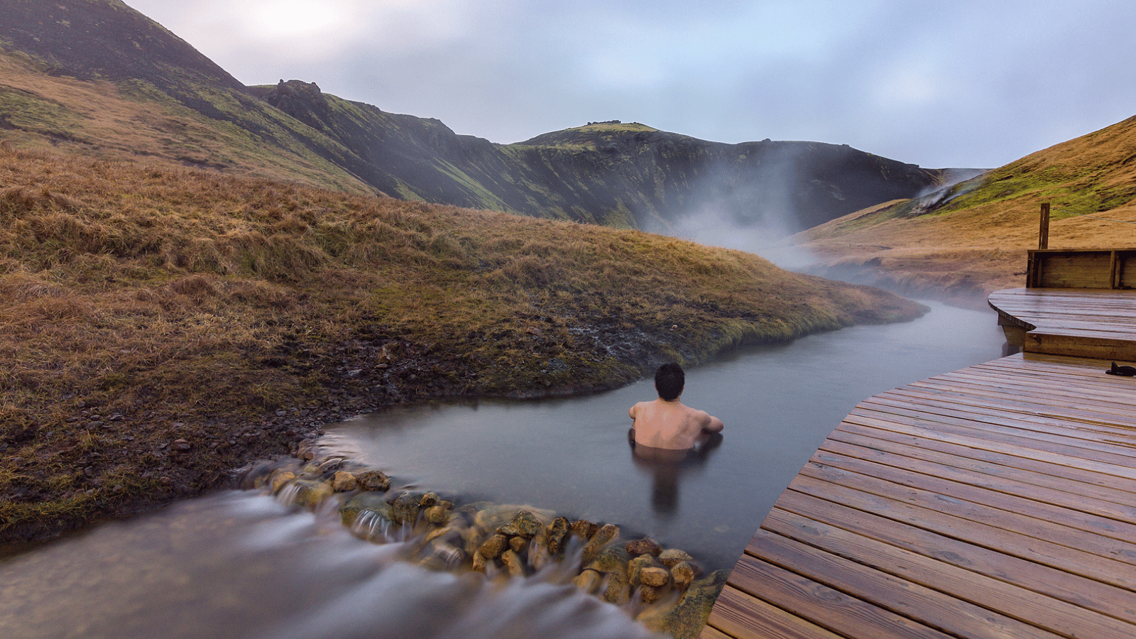 Man submerged in Reykjadalur Hot Spring beside the boardwalk.