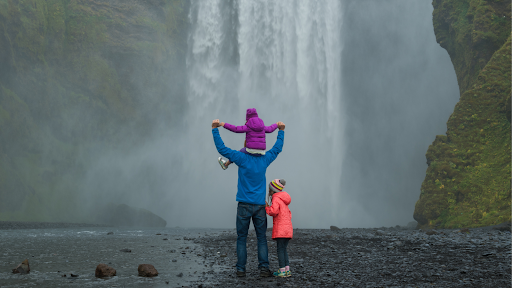Adult with kids at the base of a waterfall in Iceland