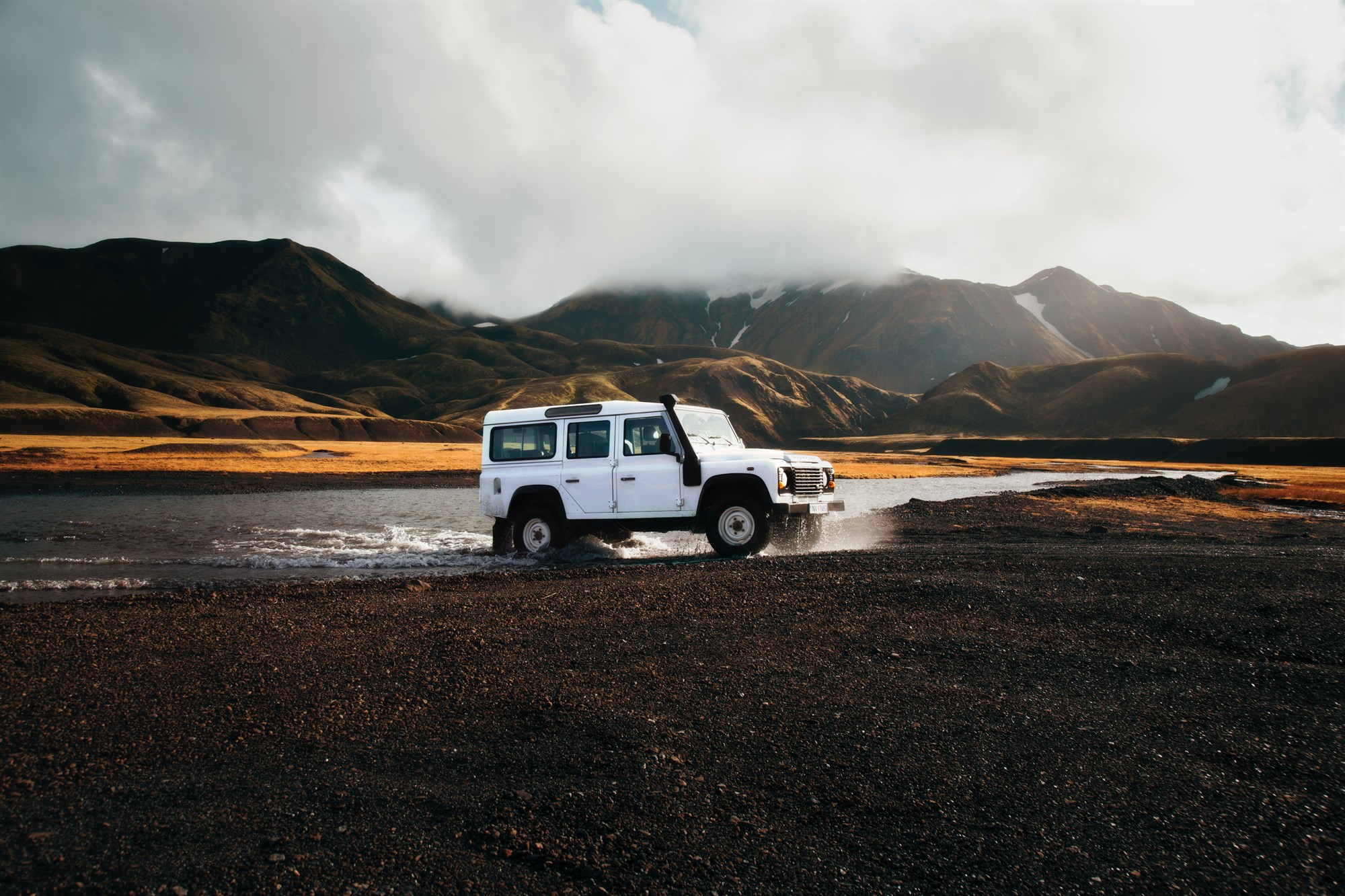 A white 4x4 vehicle fording a river in Iceland.