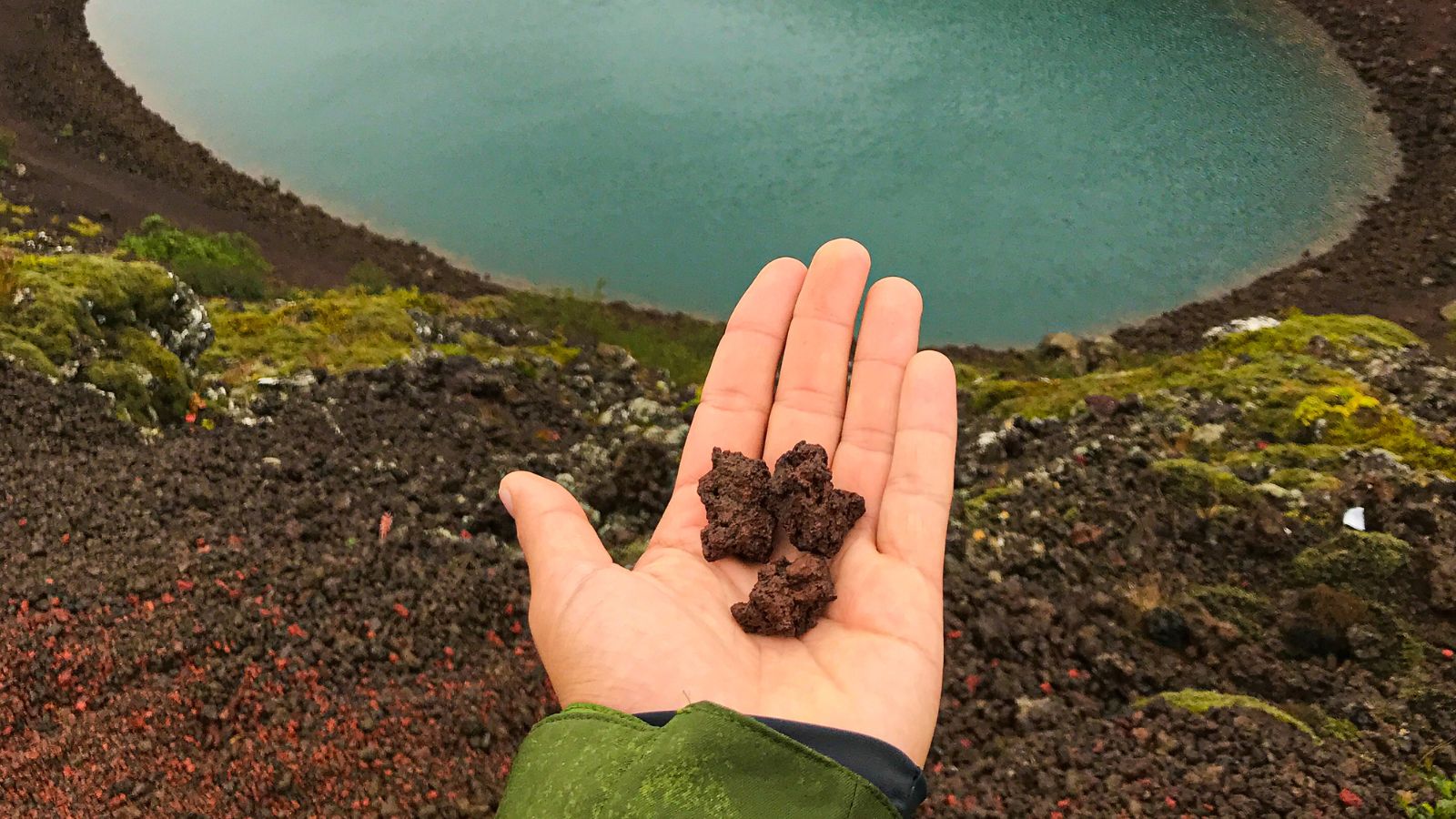 Person holding red volcanic rock at Kerid Crater Lake.