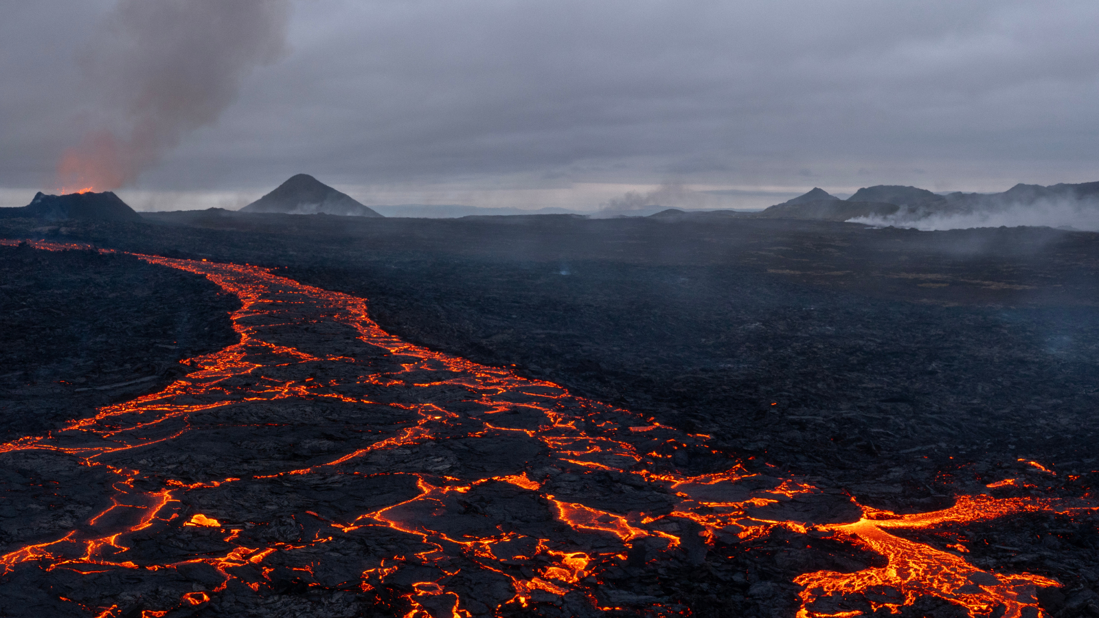 Orange highlights across a flow of lava with the Litli-Hrútur eruption on the horizon.