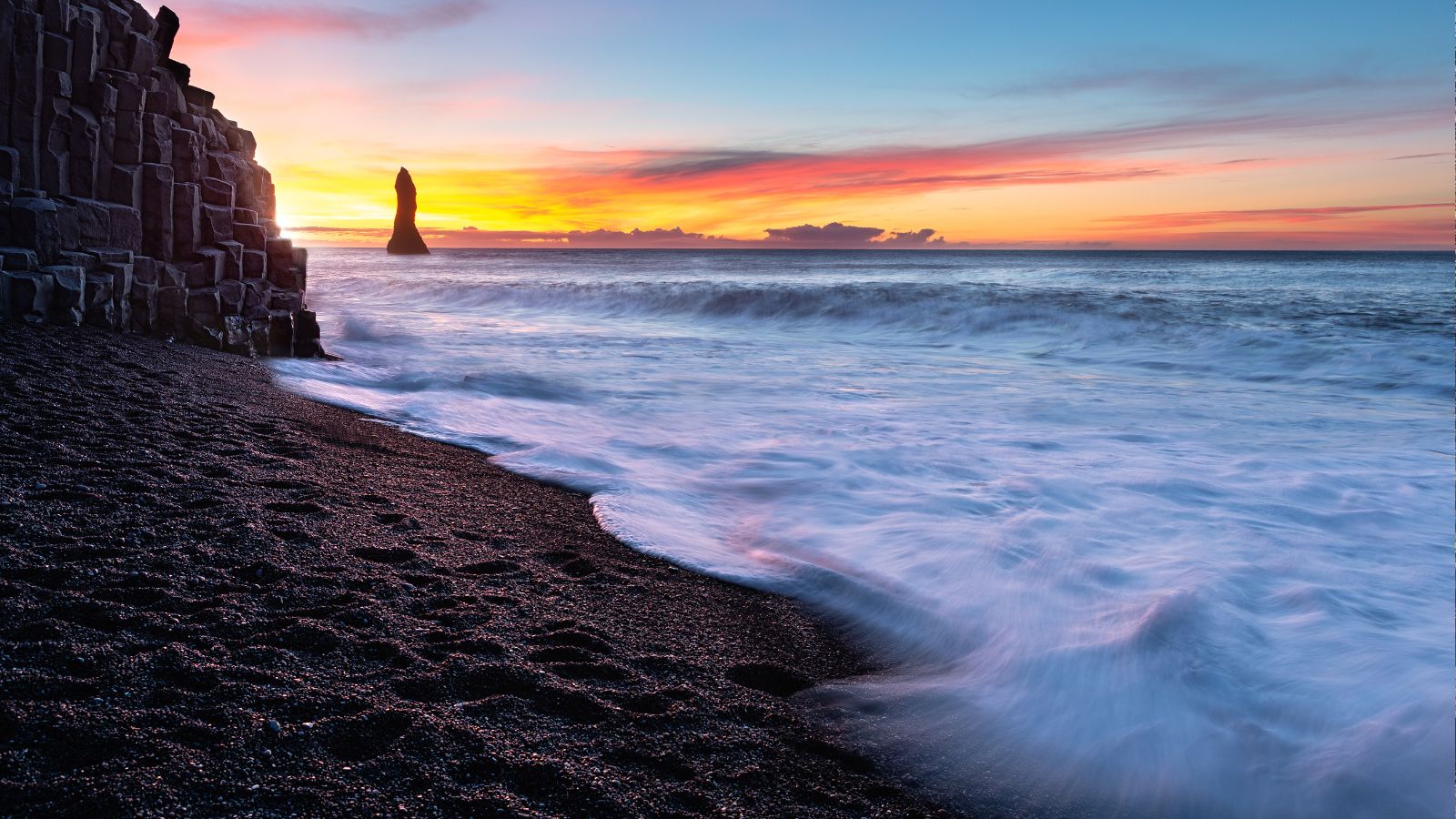 Reynisfjara Beach at sunset with a view of the basalt cliffs, surf, and Reynisdrangar sea stacks.