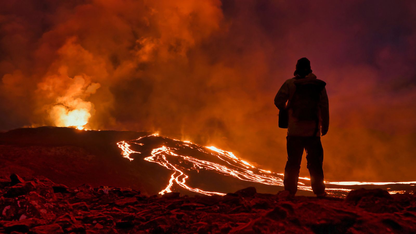 Someone observing the lava flow and eruption of Fagradalsfjall volcano in Iceland at night.